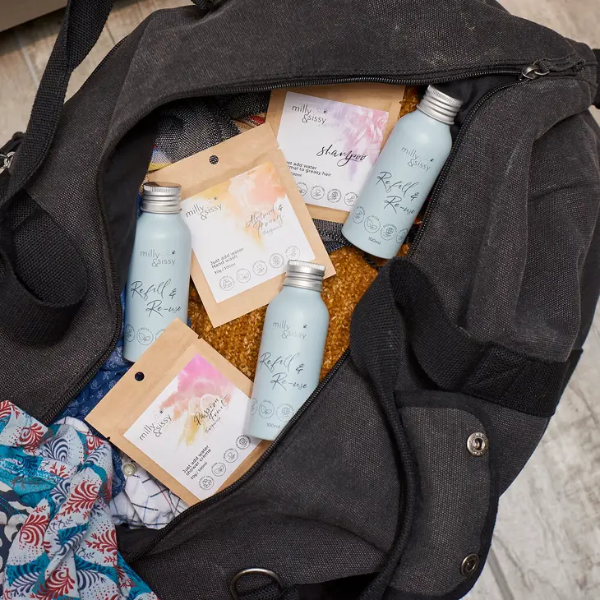 Aluminium reusable travel bottles shown inside a travel bag alongside milly & sissy refill pouches