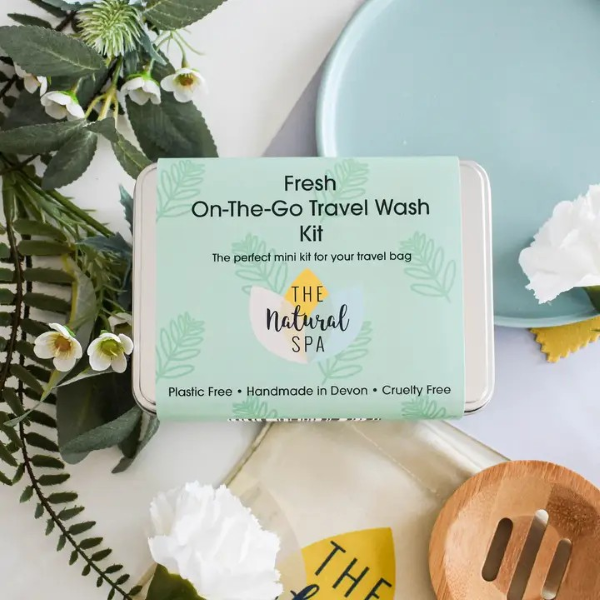 On the go travel wash kit in Fresh showing aluminium tin with green paper label on greenery alongside a wooden soapdish