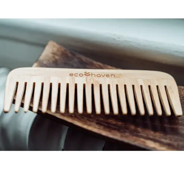 Bamboo wide-tooth comb lying on a wooden plate with logo reading ecohaven