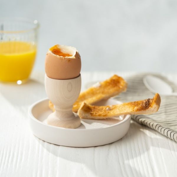 Wooden egg cup sitting on a saucer with an open soft boiled egg and some toast soldiers