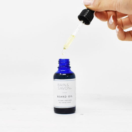Bain and Savon beard oil in blue glass bottle with hand holding the pipette containing liquid