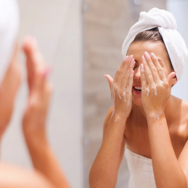 Woman in bathroom washing her face with towel on head and soap on face