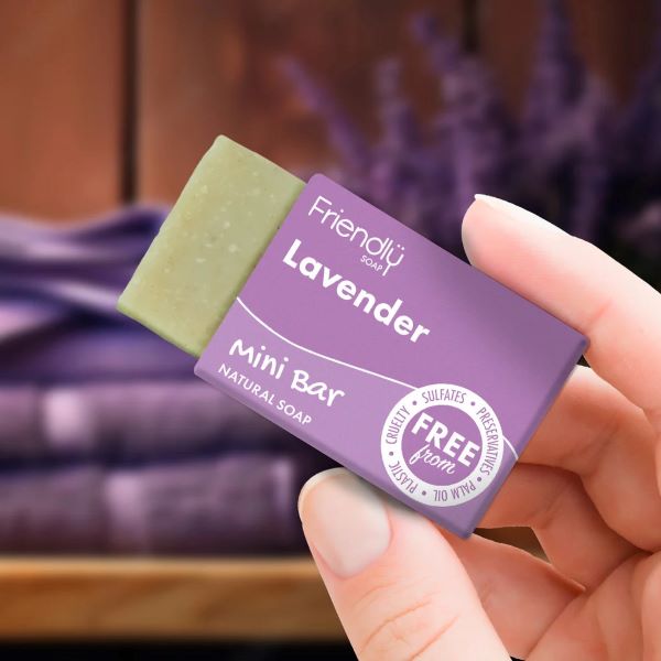 A mini vegan soap bar by Friendly Soap, lavender scent, shown in a hand holding its purple box, the soap peeking out.