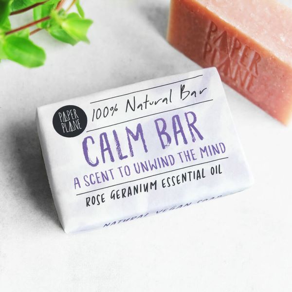 Paper Plane's calm bar showing bar and wrapping. Text on white paper wrapper reads "100% natural bar, Calm bar, a scent to unwind the mind, rose geranium essential oil"