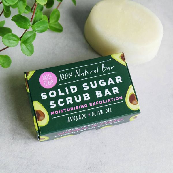 Natural sugar scrub bar shown alongside its cardboard packaging (dark green box with images of avocados) and stating "Moisturising exfoliation, avocado and olive oil"