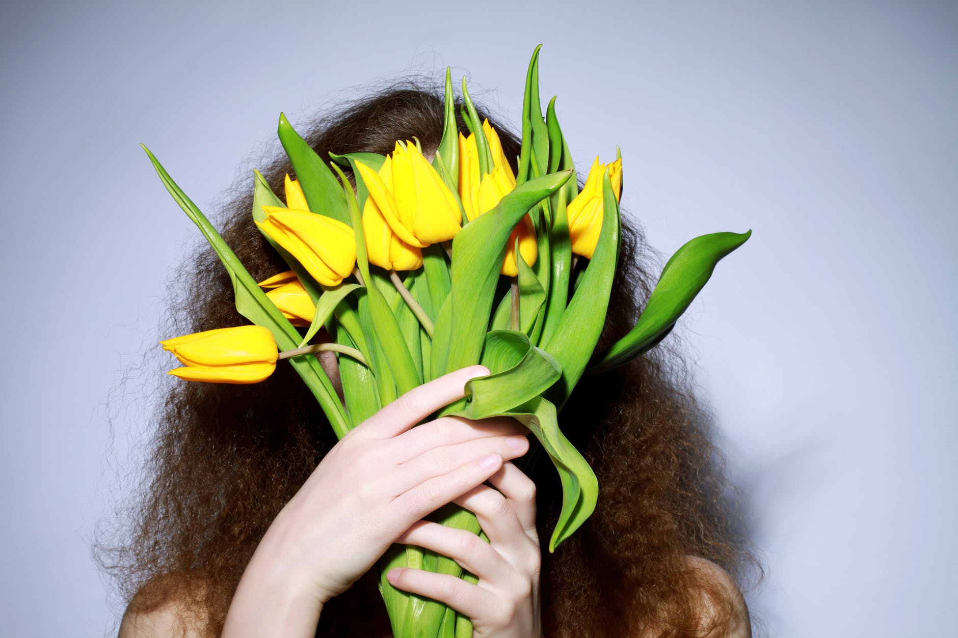 Person with long curly hair holding a bunch of yellow tulips in front of their face