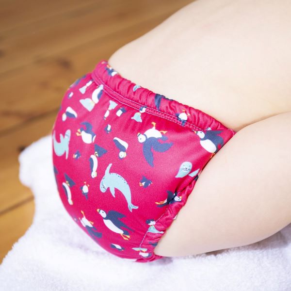 Baby wearing reusable swim pants back view in Puffling Paddle design (red background with puffins and seals)