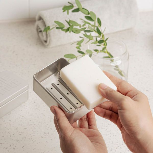 Metal travel soap case with hand popping a soap bar inside, drip tray showing