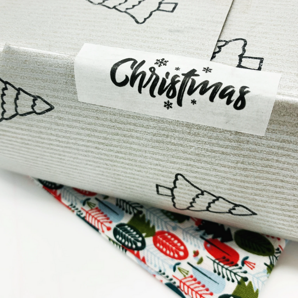 Eco-friendly paper tape White with black writing saying Christmas and little black snowflakes, on a parcel with silver paper
