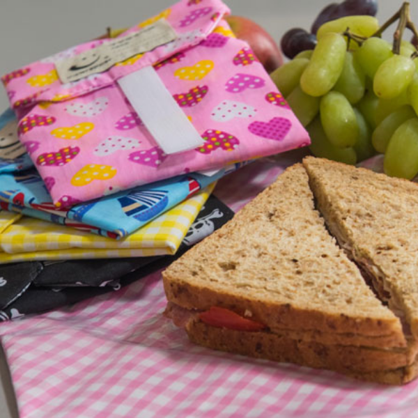 Eco-friendly sandwich wrapper in use with brown bread sandwich. Several wrappers alongside.
